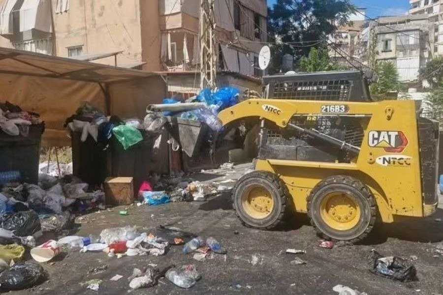 آلية تعمل بين نفايات متراكمة قرب مستوعبات في شارع سكني