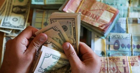 يدان تعدّان أوراقًا نقدية بالدولار أمام رزم من الليرات اللبنانية